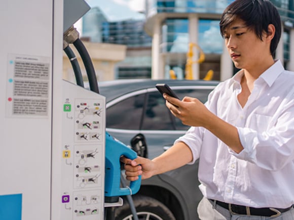 Man charging an EV at a public charging station and pays using a mobile phone
